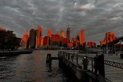 The Manhattan Financial District skyline under an orange sky, seen from Brooklyn Bridge Park.